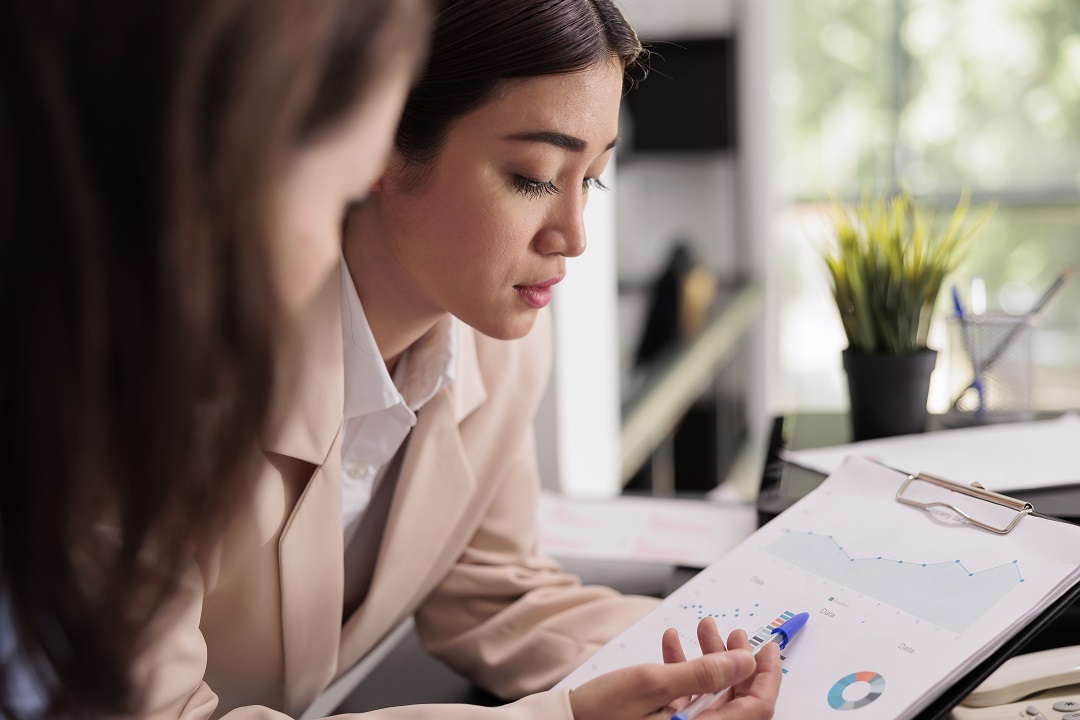 Employees analyzing financial report statistics on clipboard Front office manager conducting front desk performance review of receptionist