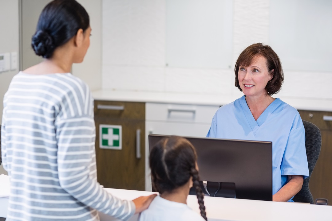 Nurse talking with a patient at counter Medical receptionist accommodating patient and parent facilitating positive patient experience for front desk performance